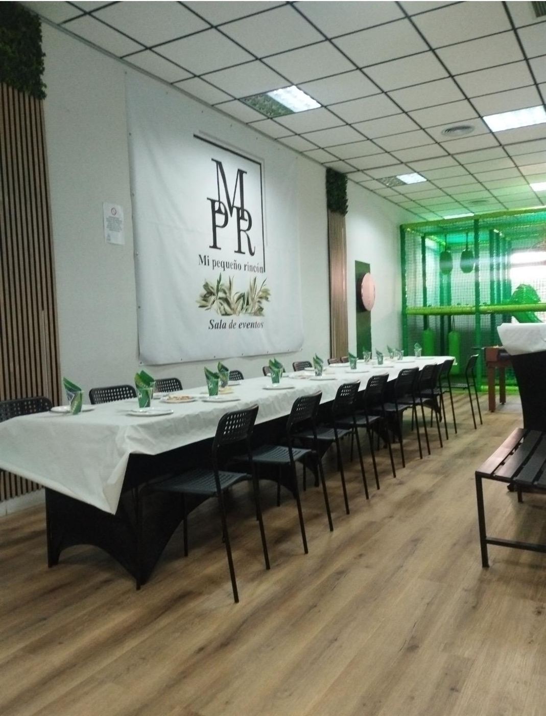 Mesa larga preparada para un evento en Mi Pequeño Rincón, con la zona de juegos infantil al fondo